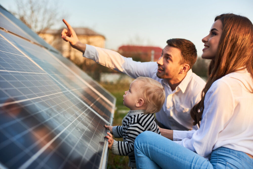 Famille heureuse devant maison avec panneaux solaires, signifiant sérénité et économies
